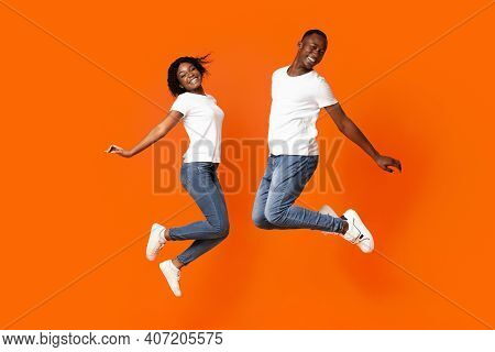Lifefull African American Young Handsome Man And Pretty Woman Jumping Up Over Orange Studio Backgrou