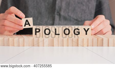The Hand Puts A Wooden Cube With The Letter A From The Word Apology. The Word Is Written On Wooden C
