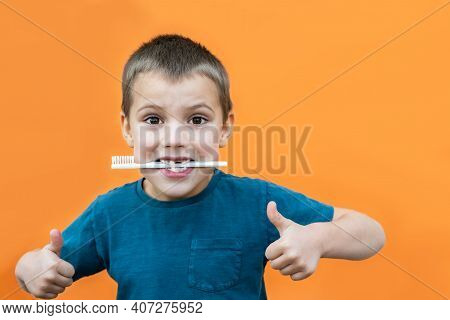 Boy Without Milk Upper Tooth In Blue T-shirt Holds Toothbrush In His Mouth On The Orange Background.