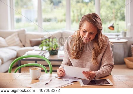 Woman With Digital Tablet Sitting At Table At Home Reviewing Domestic Finances