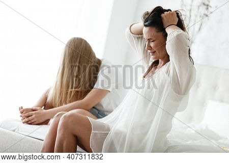 Family conflict and relations concept. Mother and daughter having quarrel and aguring at home. Sad woman and teenage girl sitting on bed. Not looking at each other.