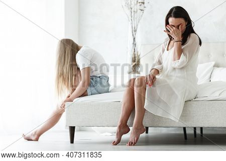 Family conflict and relations concept. Mother and daughter having quarrel and aguring at home. Sad woman and teenage girl sitting on bed. Not looking at each other.