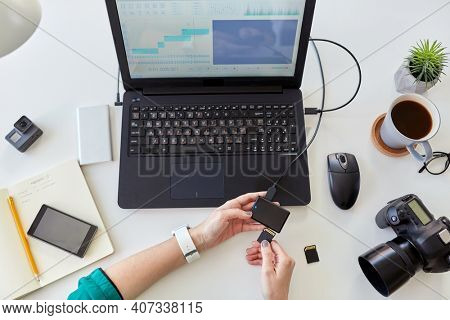 technology, post production and vlog concept - close up of woman with sd memory card reader working in video editor program on laptop computer working at home office
