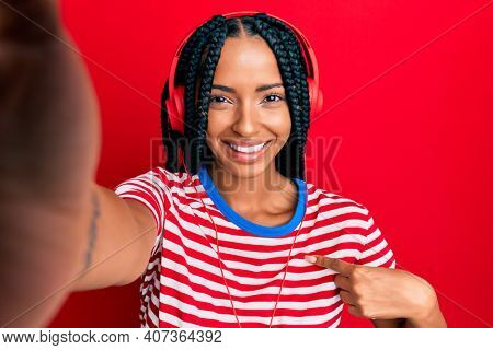 Beautiful hispanic woman taking a selfie photo wearing headphones pointing finger to one self smiling happy and proud 