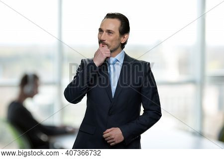 Portrait Of Thougtful Boss Is Standing In Offce. Businessman In Formal Suit And Thinking About Somet