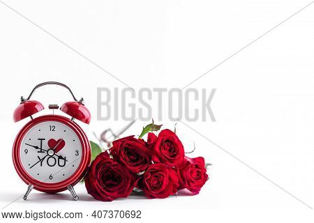 Red Alarm Clock With A Bouquet Of Fresh Red Roses On A White Background. Greeting Card For Valentine
