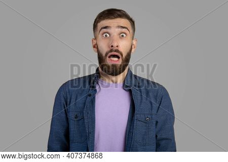 Shocked Bearded Guy Looking At Camera In Panic Over Grey Studio Background. Frightened Young Man Fee