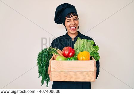 Beautiful brunettte woman chef holding fresh veggetables winking looking at the camera with sexy expression, cheerful and happy face. 
