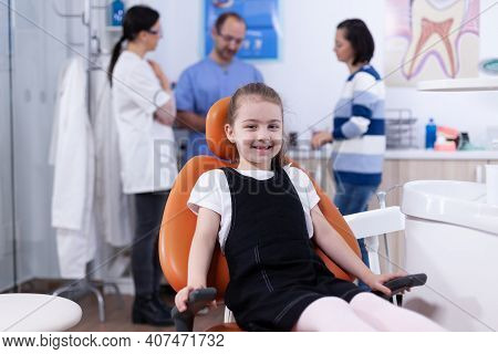 Little Girl With Missing Tooth Sitting On Chair In Dentist Office Smiling At Camera. Child With Her 