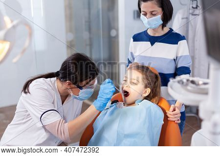 Stomatolog Using Angled Mirror During Oral Examining Of Girl Sitting On Dental Chair. Dentistry Spec