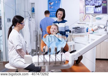 Little Girl In Pediatric Dentist Office Touching Face With Painful Expression Because Of Tooth Healt