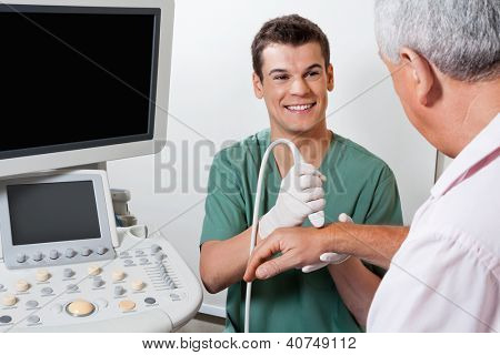 Mužské radiologické technik s úsměvem při prohledávání mužský pacient ruku na klinice