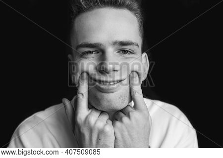 A Young Guy, A Teenager, Keeps His Fingers On His Cheeks, In Stress Tries To Force Himself To Smile.