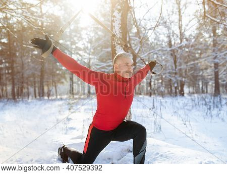 Fitness Suspension Training Concept. Athletic Senior Man Working Out With Sports Equipment On Snowy 