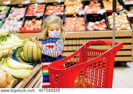 Cute Todler Girl With Medical Mask Pushing Shopping Cart In Supermarket. Little Child Buying Fruits.