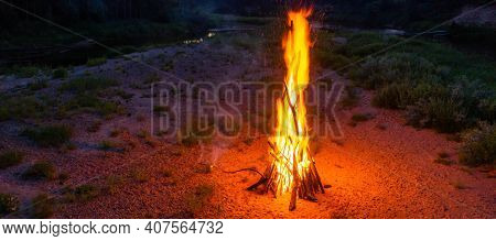 Midsummer Ligo Celebration. Huge Bonfire On The River Shore. Scenic Landscape Of Forest. Sunset Sky.