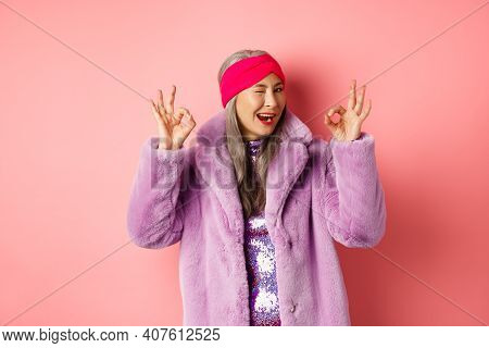Fashion And Shopping Concept. Stylish Asian Granny Saying All Okay And Winking. Trendy Senior Woman 
