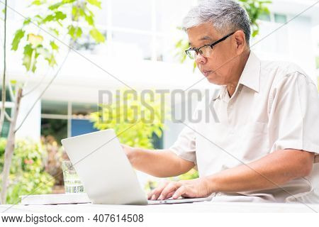 Portrait Of Old Elderly Asian Man Using A Computer Laptop In The Backyard For Learning New Skill Aft