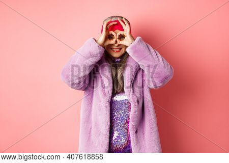 Fashion And Shopping. Happy Asian Grandmother In Stylish Faur Fur Coat, Looking Through Hand Glasses