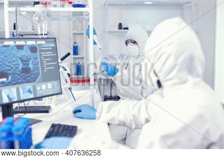 Experienced Doctor Taking Sample From Test Tube Using Micropipette Wearing Sterile Suit. Team Of Mic