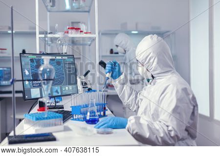 Concentrated Scientist Using Micropipette With A Test Tube And Coworker Standing In The Background. 