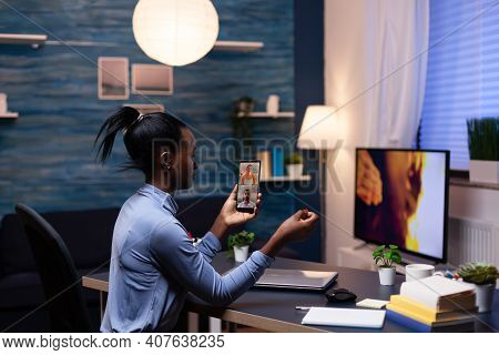 Woman With Dark Skin Holding Phone In Online Meeting Sitting At Desk In Hime Office Late At Night. B