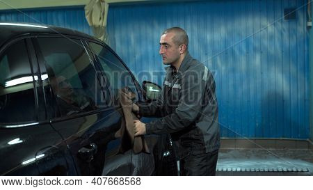 A Caucasian Man Works In A Car Wash Service. A Man In A Workers Uniform Is Wiping His Car With A Rag