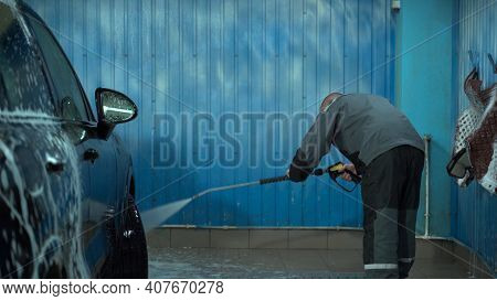 A Caucasian Man Works In A Car Wash Service. A Man In A Worker's Uniform Washes The Car Thoroughly B