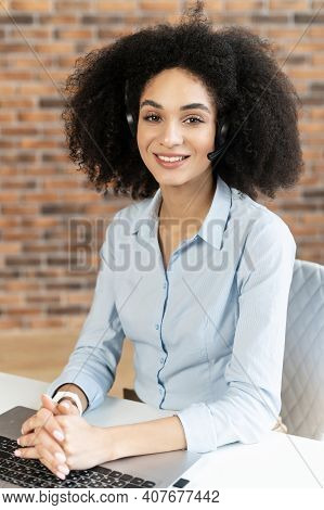 Formal Portrait Of An Intelligent Young Mixed-race Woman With Afro Hairstyle In Headset Smiling, Sit