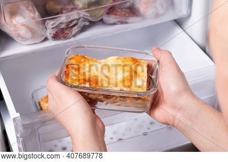 A Person Is Taking A Container Of Frozen Casserole Or Lasagne Out Of The Freezer. Concept Of Ready M