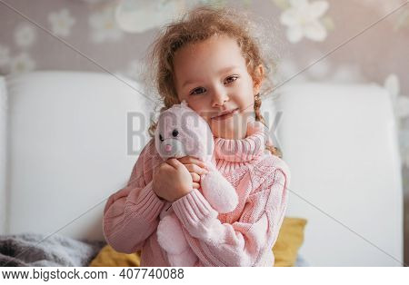 Little Cute Girl Hugs A Soft Toy In A Room On The Bed