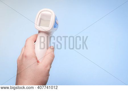 Infrared Thermometer On A Blue Background In Your Hand. The Thermometer In His Hand . Prevention. No