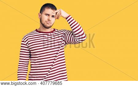 Young handsome man wearing striped sweater pointing unhappy to pimple on forehead, ugly infection of blackhead. acne and skin problem 