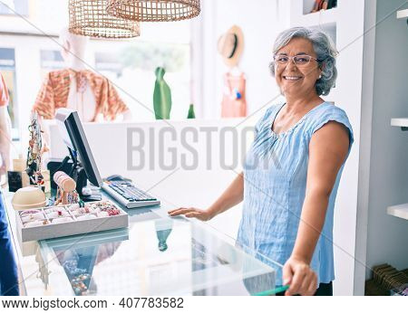 Middle age shop assistance woman working at the counter of retail shop smiling happy