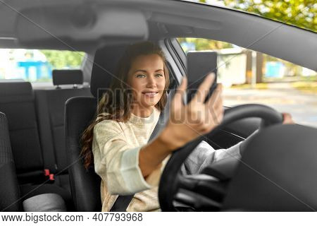 safety and people concept - happy smiling young woman or female driver driving car and taking selfie with smartphone