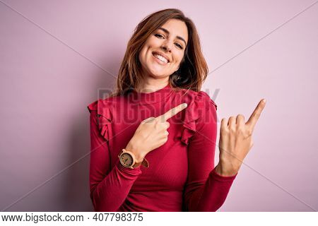 Young beautiful brunette woman wearing casual sweater stnding over pink background smiling and looking at the camera pointing with two hands and fingers to the side.