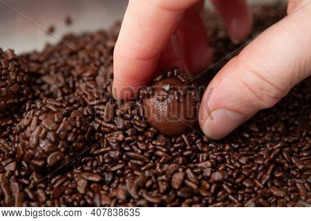 Hand Picking Up Brigadeiro On Aluminum Tray. The Brigadeiro Is A Traditional Brazilian Dessert. Clos