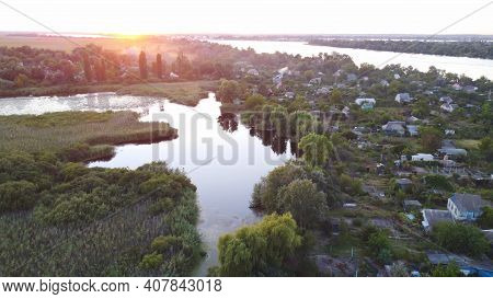 Drone Fly Over Waving River Of Blue Color Surrounded By Local Village With Various Buildings And Wet