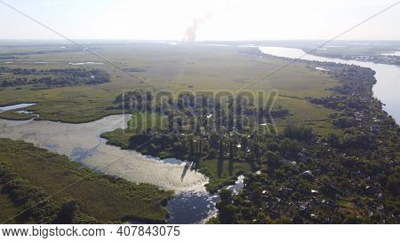Drone Fly Over Waving River Of Blue Color Surrounded By Local Village With Various Buildings And Wet
