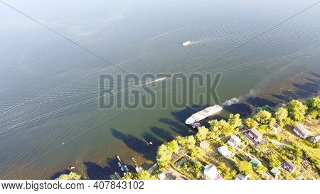Drone Fly Over Waving River Of Blue Color Surrounded By Local Village With Various Buildings And Wet