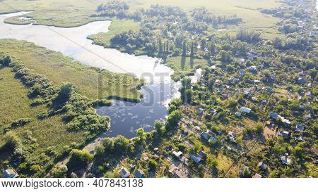 Drone Fly Over Waving River Of Blue Color Surrounded By Local Village With Various Buildings And Wet
