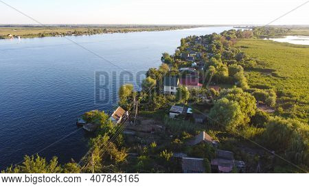 Drone Fly Over Waving River Of Blue Color Surrounded By Local Village With Various Buildings And Wet