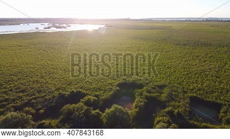 Drone Fly Over Waving River Of Blue Color Surrounded By Local Village With Various Buildings And Wet