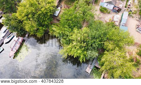Drone Fly Over Waving River Of Blue Color Surrounded By Local Village With Various Buildings And Wet