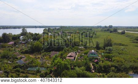 Drone Fly Over Waving River Of Blue Color Surrounded By Local Village With Various Buildings And Wet