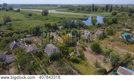 Drone Fly Over Waving River Of Blue Color Surrounded By Local Village With Various Buildings And Wet