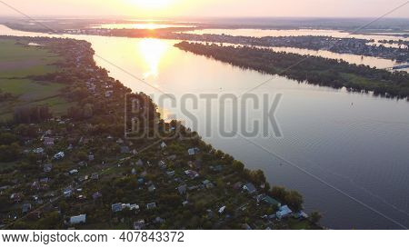 Drone Fly Over Waving River Of Blue Color Surrounded By Local Village With Various Buildings And Wet