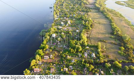 Drone Fly Over Waving River Of Blue Color Surrounded By Local Village With Various Buildings And Wet