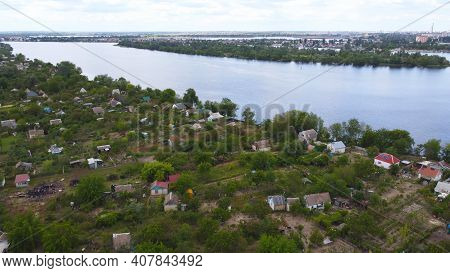 Drone Fly Over Waving River Of Blue Color Surrounded By Local Village With Various Buildings And Wet