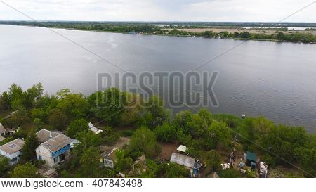 Drone Fly Over Waving River Of Blue Color Surrounded By Local Village With Various Buildings And Wet